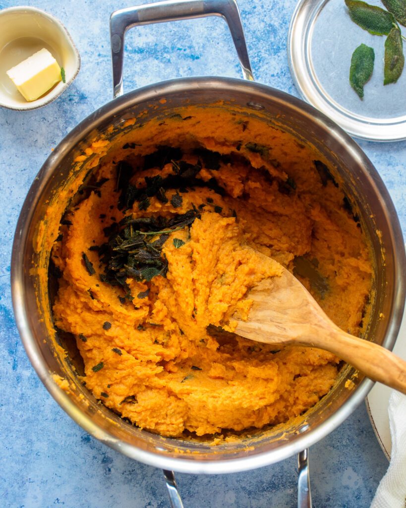 Looking down into a pot of mashed sweet potatoes with crumbled fried sage leaves in it.