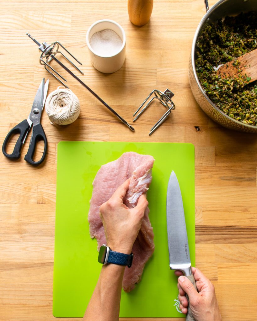 A hand turning over a butterflied turkey breast on a green cutting board.