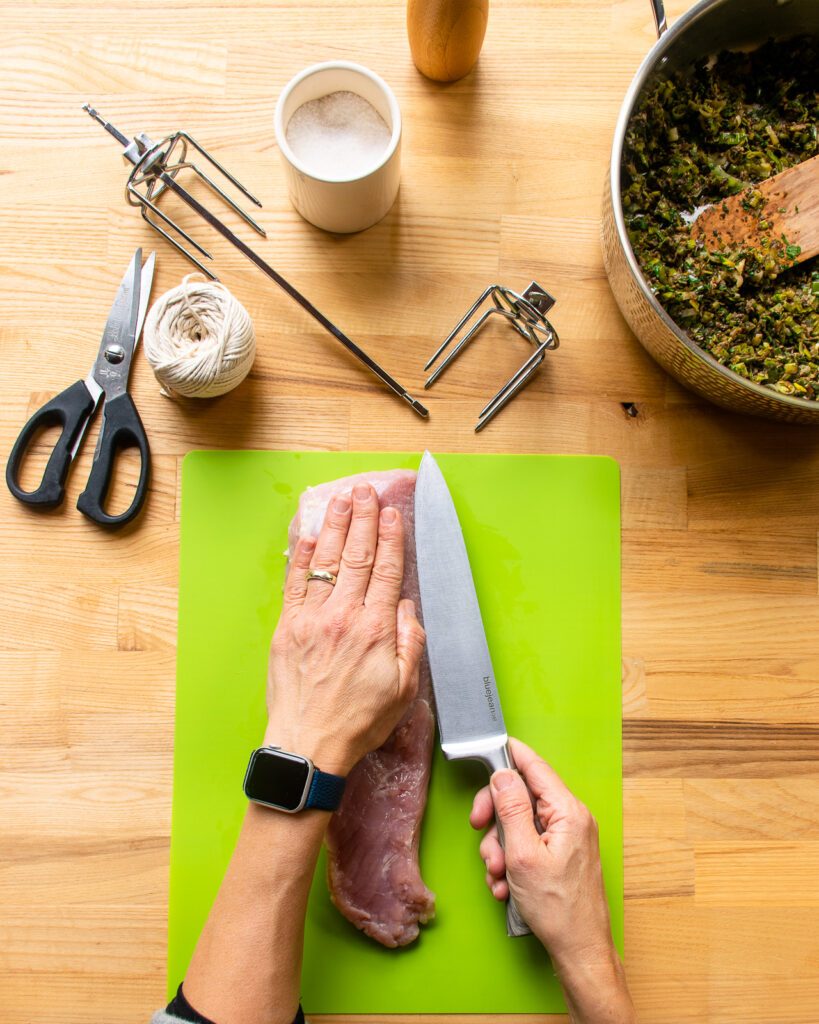A hand pressing down on a turkey breast while a knife slices into the breast parallel to the cutting board.
