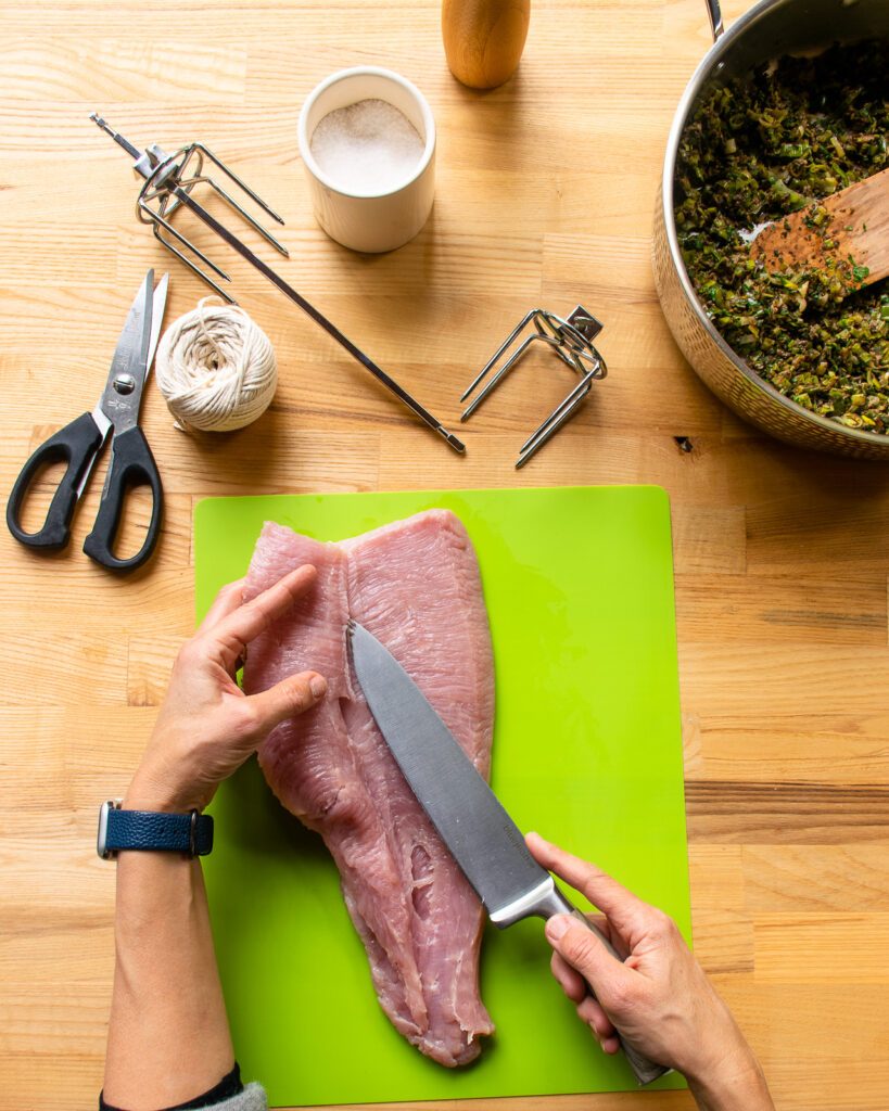 A hand opening up a butterflied turkey breast to show where the knife has cut.