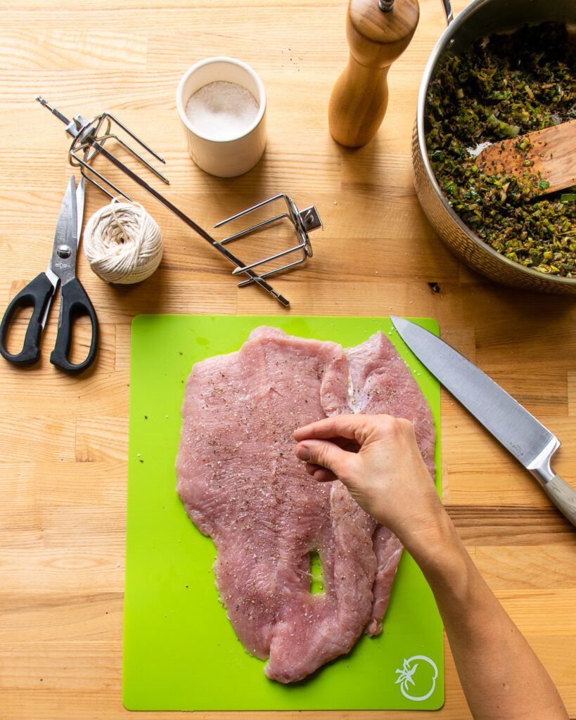 Seasoning a double-butterflied turkey breast on a green cutting board.