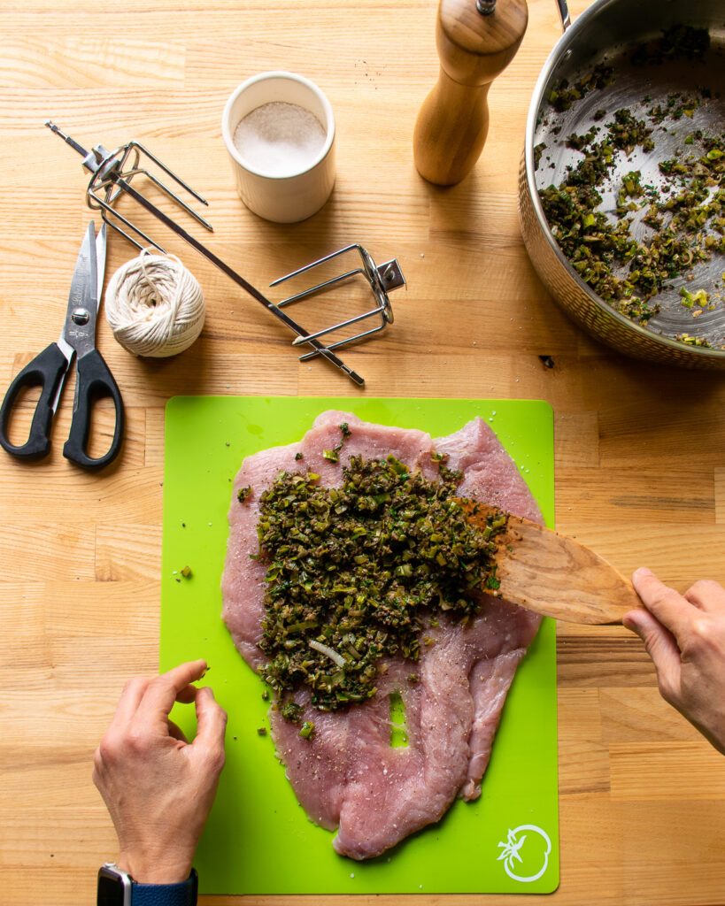 Spreading a filling on a butterflied turkey breast on a green cutting board.