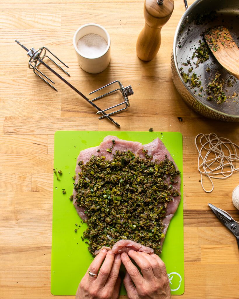 Hands starting to roll up a double-butterflied turkey breast with a filling inside.