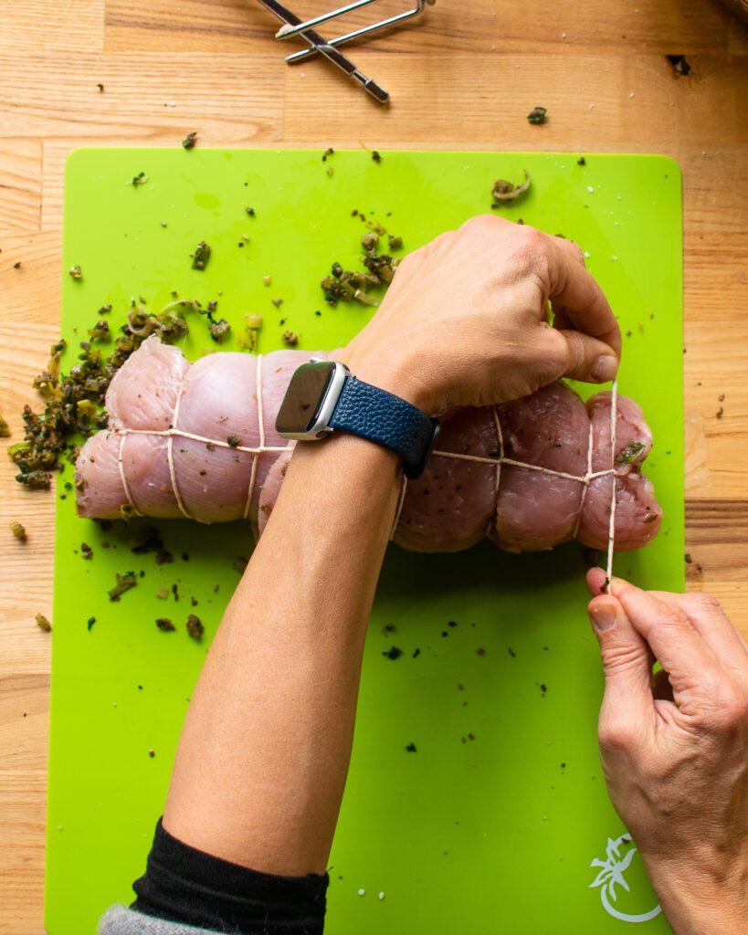 Two hands tying the last piece of twine on a turkey breast. 