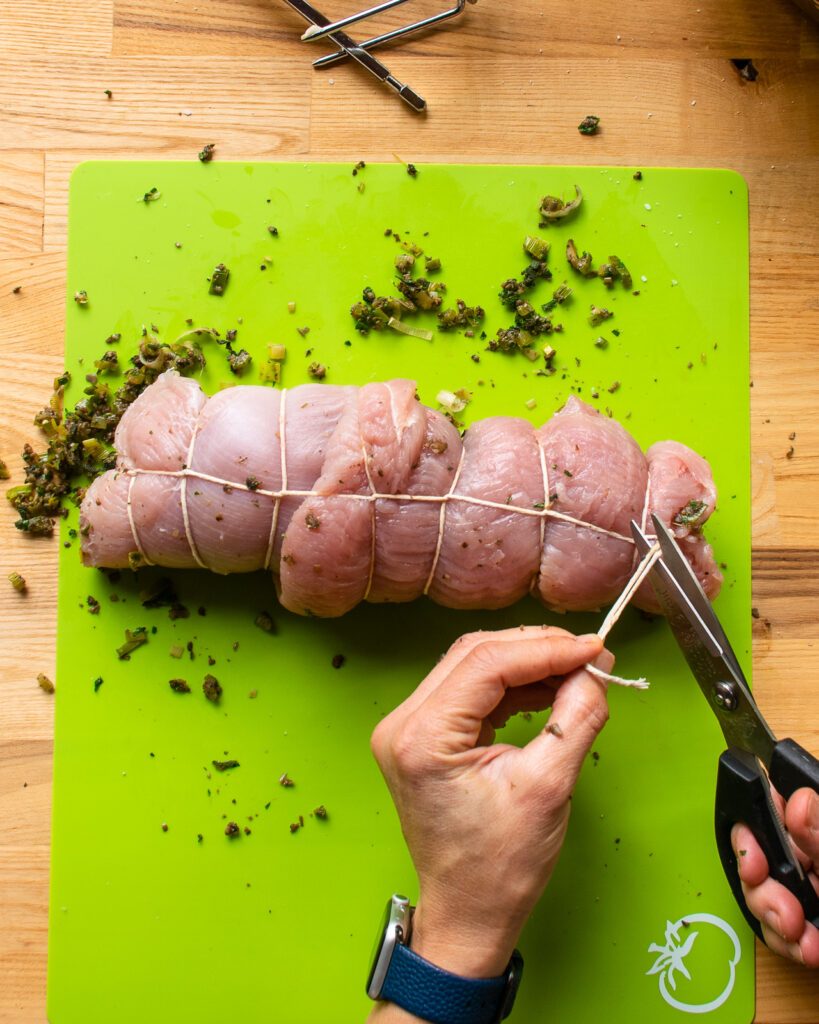 A pair of scissors cutting the ends of twine on a turkey roulade.