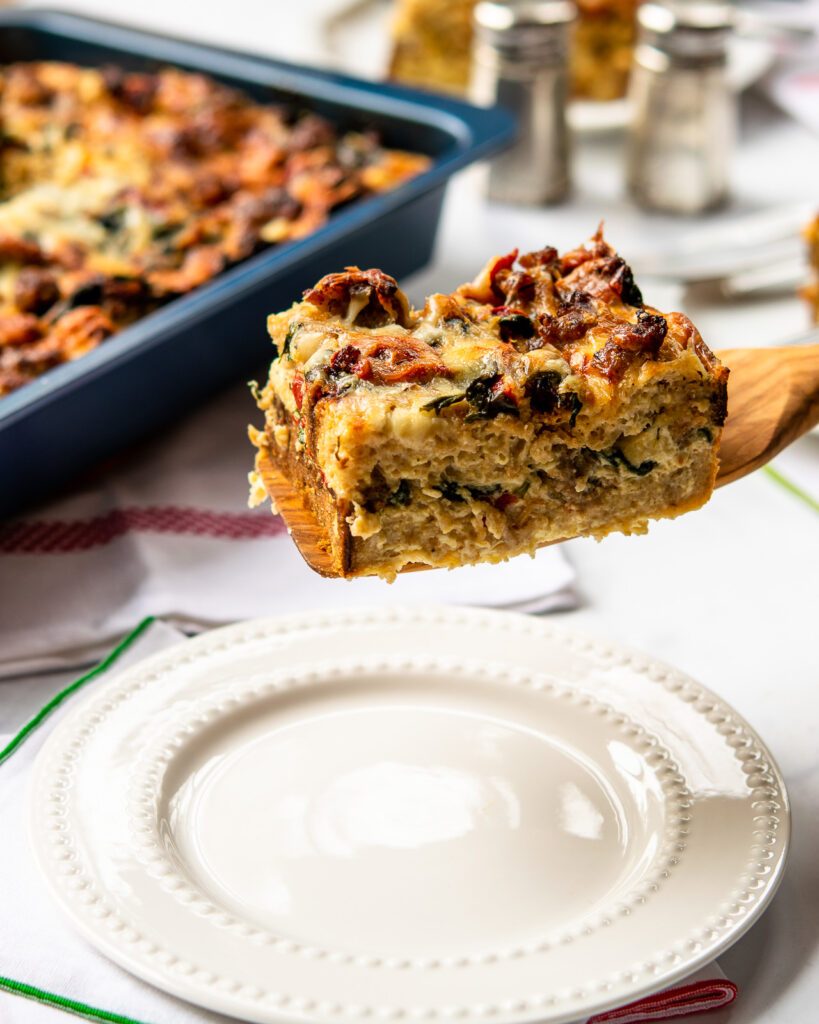 A wooden spatula serving a portion of breakfast strata onto a white plate.