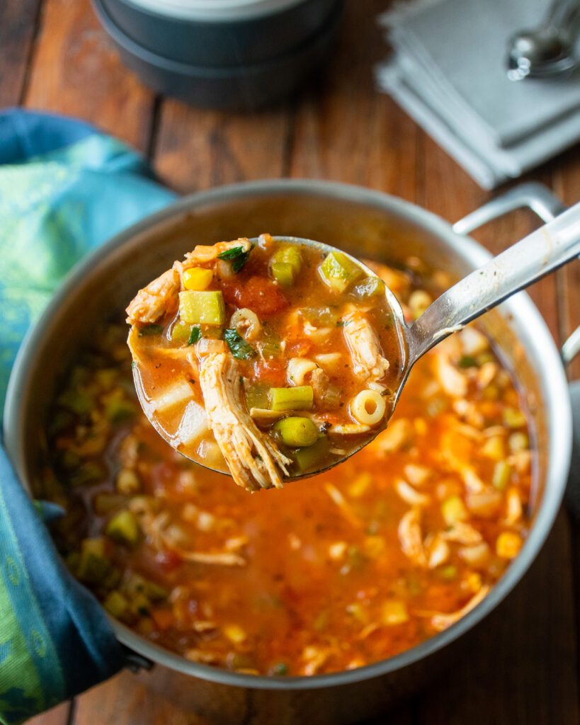 A ladle of chicken vegetable soup being held up above a stockpot of the soup.