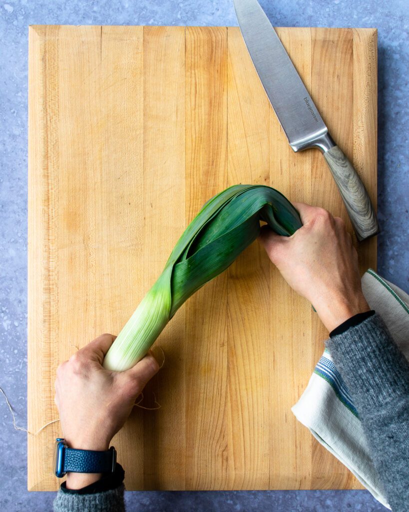 Hands bending the leaves of a leek back over a cutting board.