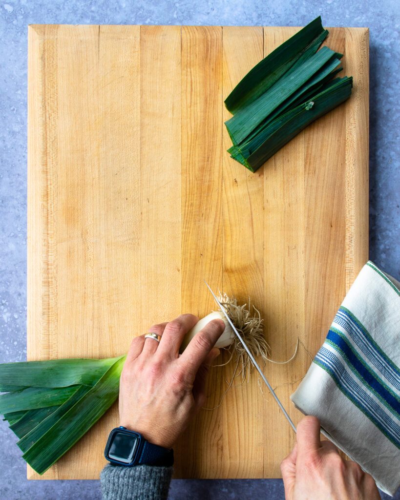 Hands trimming the roots off a leek.