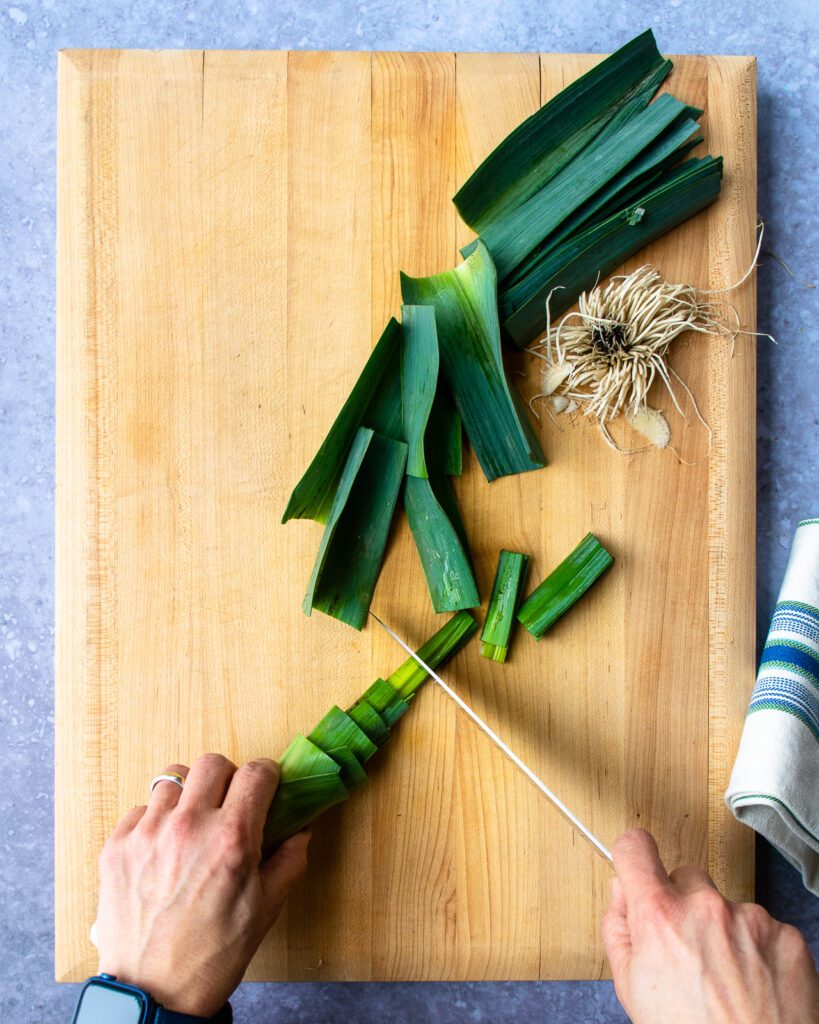 Hands trimming a leek with a chef's knife.