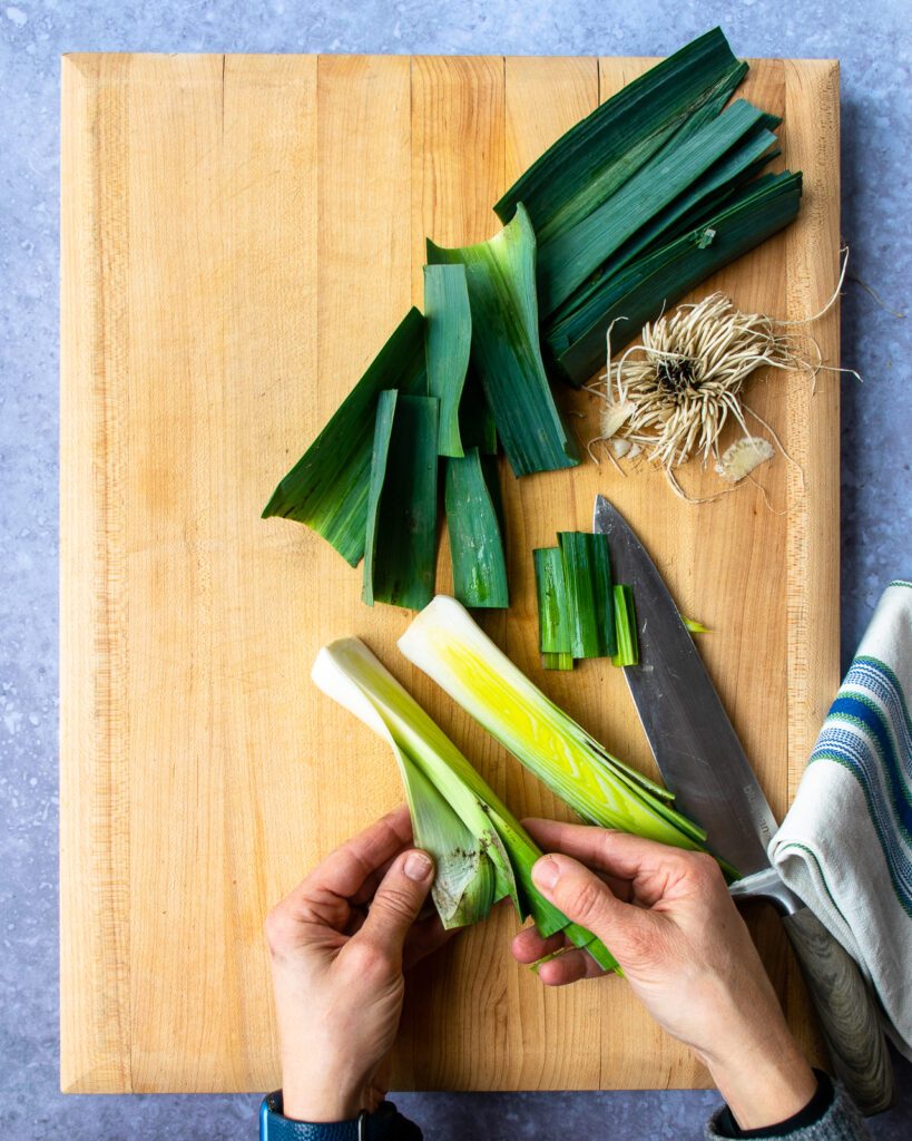 Hands spreading the leaves of a leek apart revealing dirt.