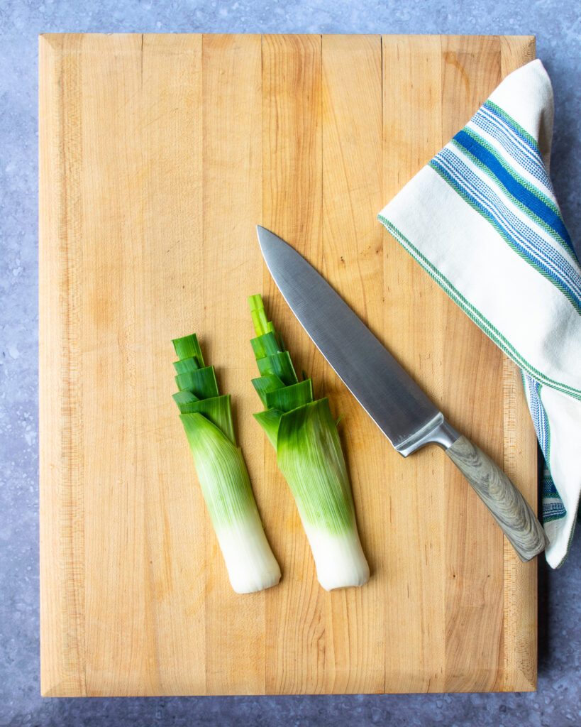 Two halves of a leek on a cutting board with a chef's knife beside them.