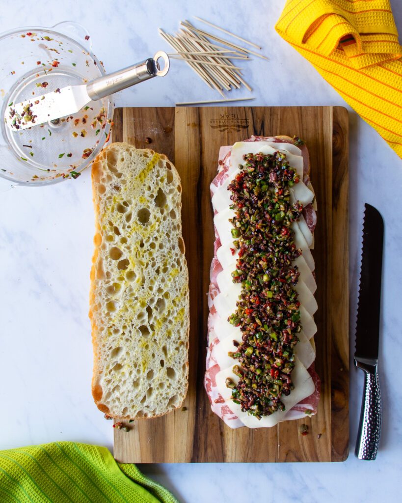 Looking down on an open muffaletta sandwich on a cutting board.