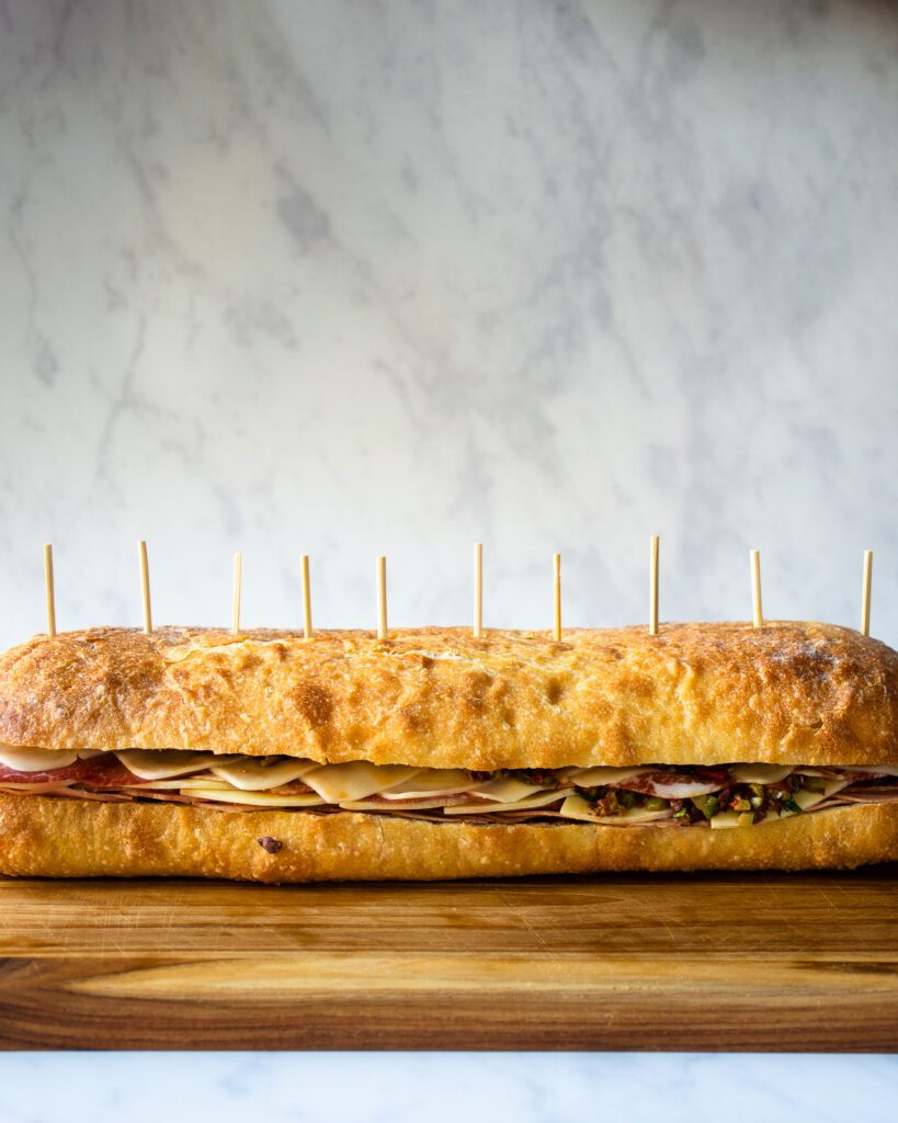 A large muffaletta sandwich on a cutting board with toothpicks inserted in the top about an inch apart.