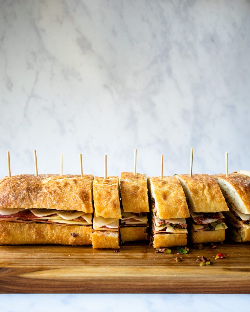 Mini muffaletta sandwiches being cut into slices on a cutting board.