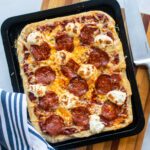A cooked pizza on a baking sheet on a cutting board with a knife and towel next to it.