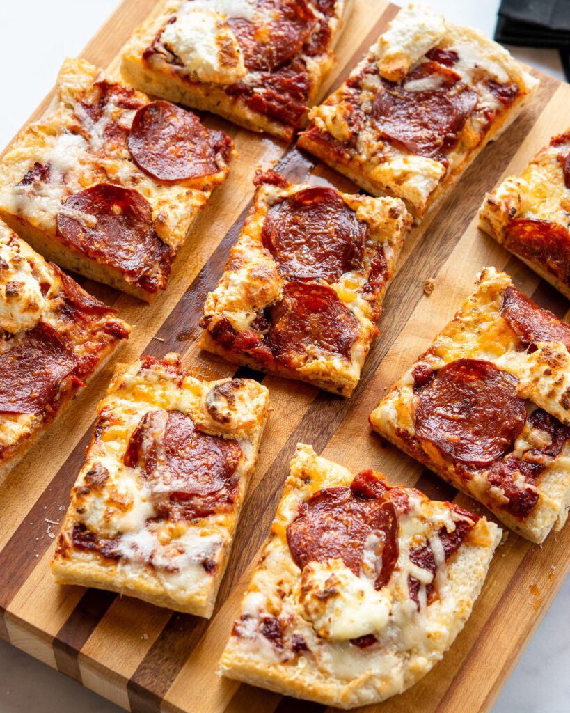 A cooked pizza cut into 9 pieces on a cutting board.