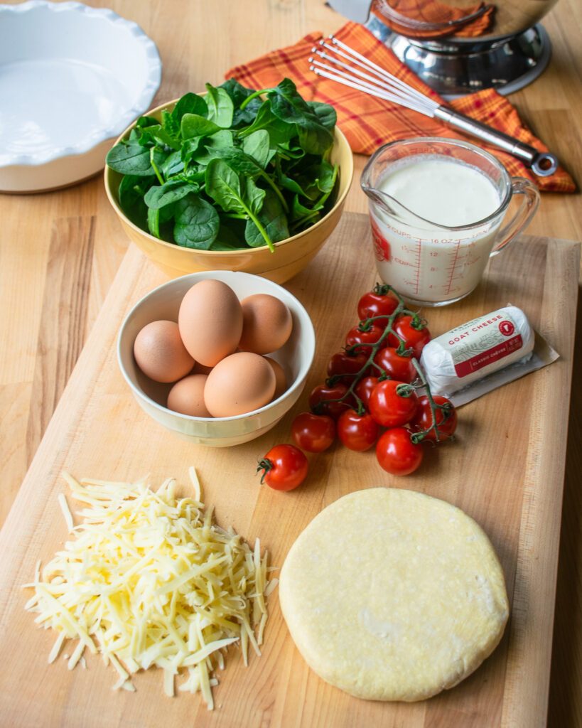 Ingredients on a cutting board - pastry, cheese, tomatoes, eggs, cream and spinach.