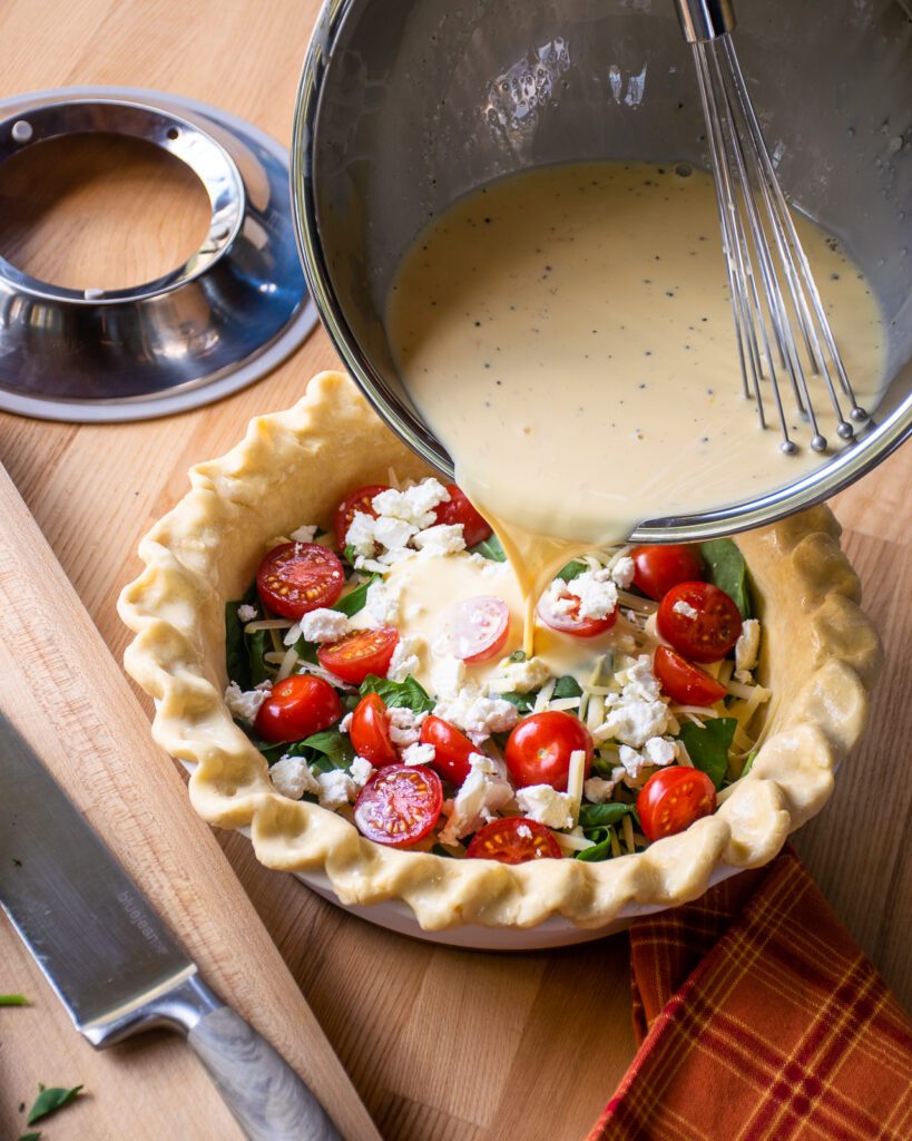 Pouring egg custard into a pastry crust with tomatoes, spinach and cheese inside.
