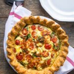 A baked quiche florentine on a wooden table with a red checkered kitchen towel and a white plate.