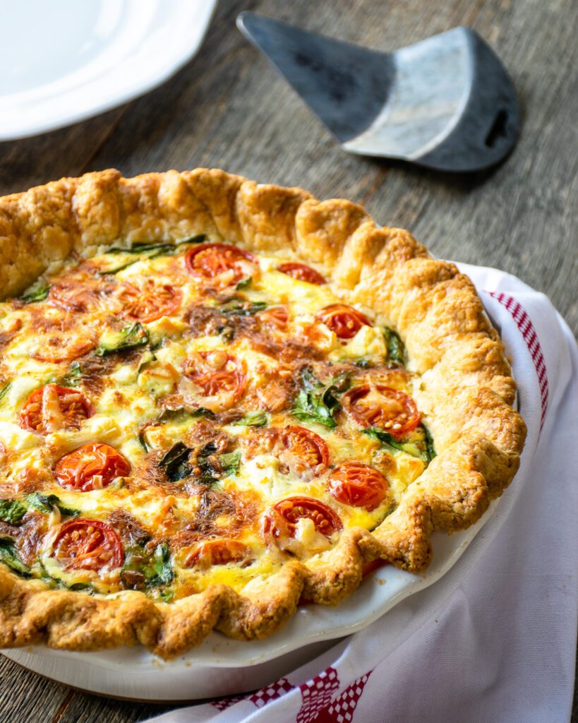 A close up of quiche florentine on a wooden table with a pie server in the background.