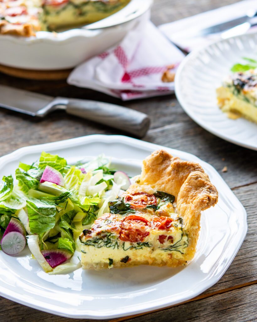 A piece of Quiche Florentine on a white plate with salad on the side.