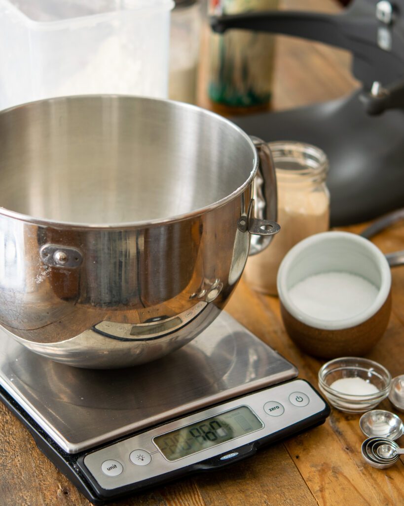 A stand mixer bowl sitting on a scale with some ingredients around.
