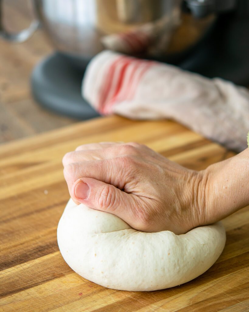 A hand kneading a ball of dough on a cutting board.