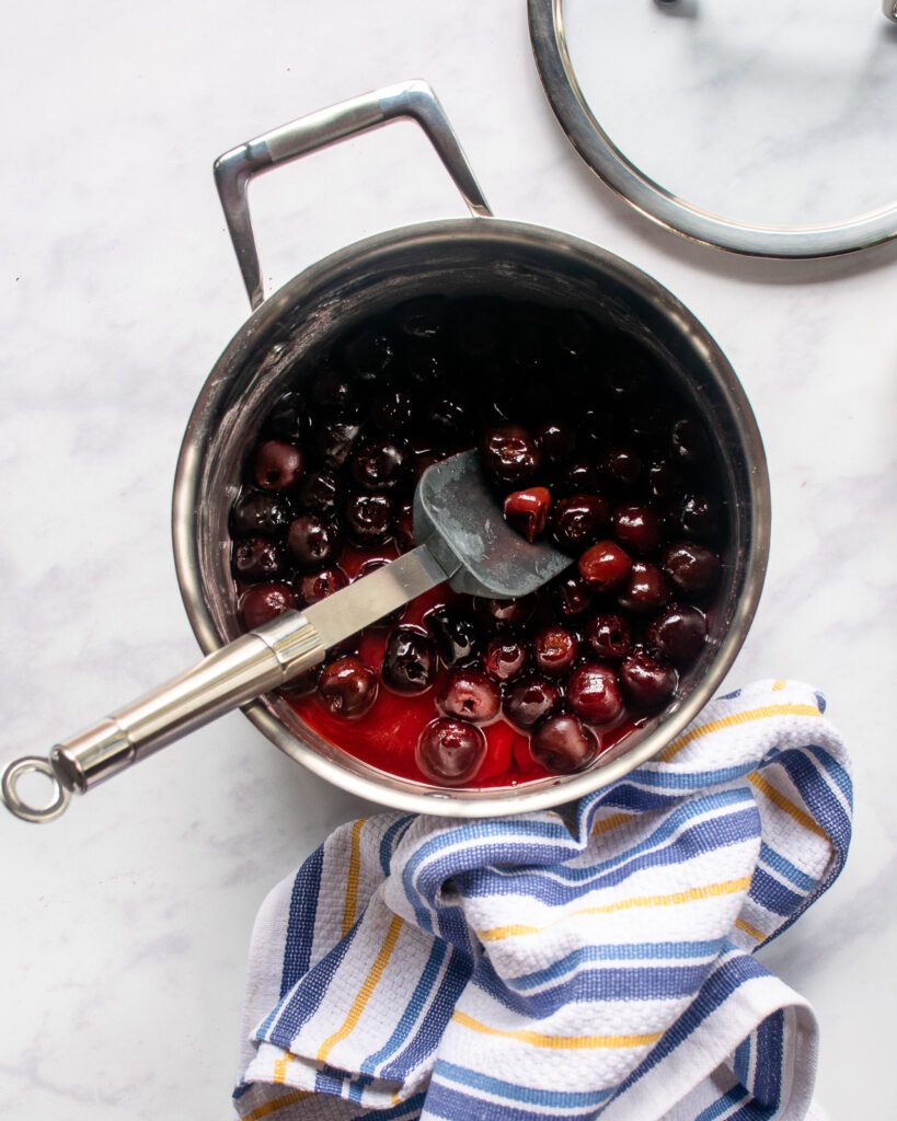 A spatula sticking out of a pan with cherries inside - the topping for black forest cheesecake.