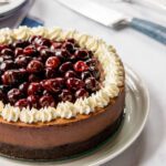 Partial view of a black forest cheesecake with a knife and cake server in the background.