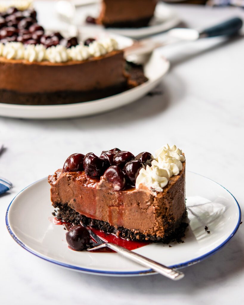 A close up of a slice of black forest cheesecake on a blue rimmed white plate.