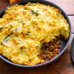 Shepherd's Pie in a skillet with portion scooped out on a wooden table.