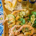 Tequila lime shrimp on a board with shot glasses of tequila, lemon wedges and salt.