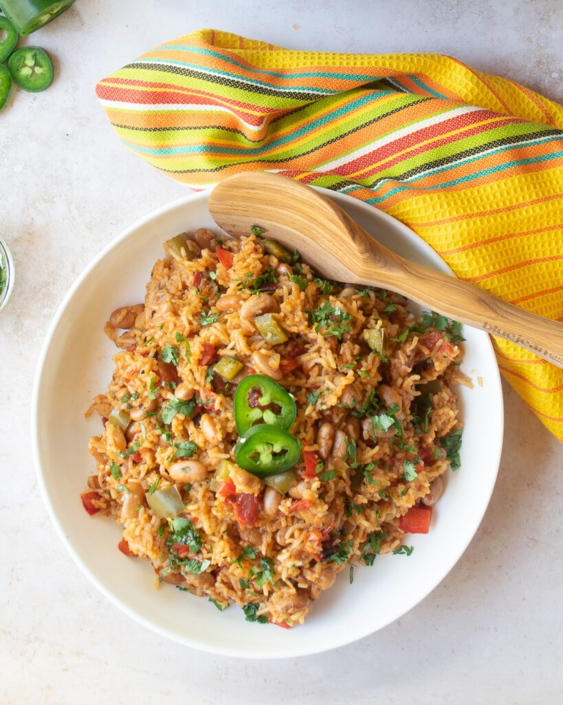 Mexican rice and beans in a white bowl with wooden spoon and yellow kitchen towel.