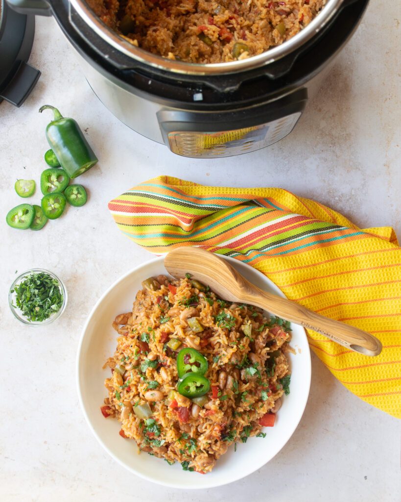 Mexican rice and beans in a white bowl with wooden spoon and yellow kitchen towel.