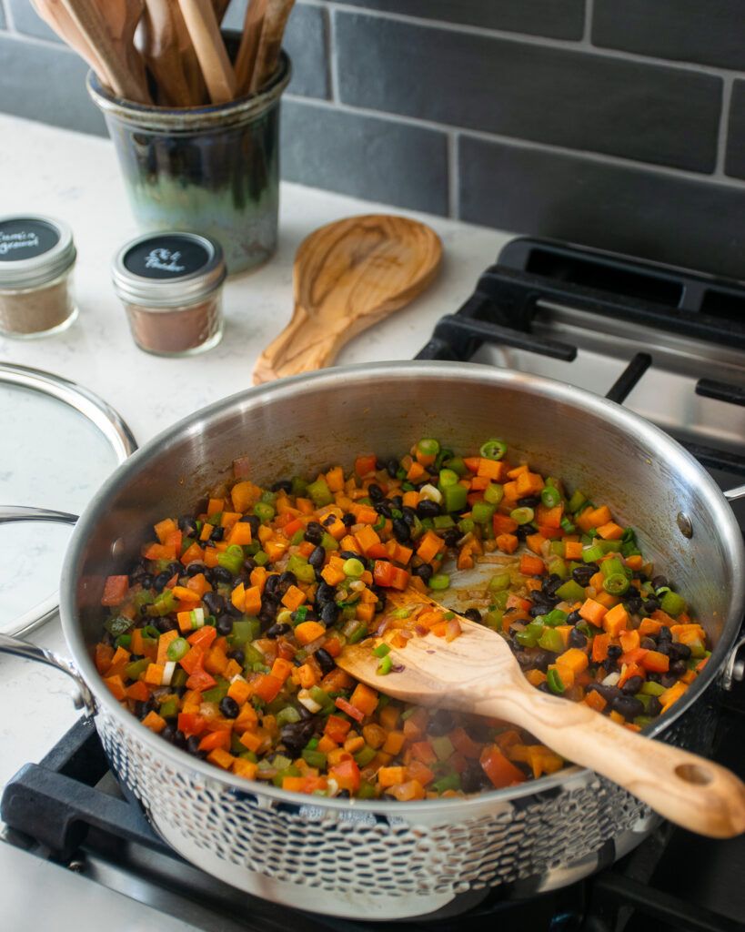 Diced vegetables cooking on the stovetop in a stainless steel saute pan.