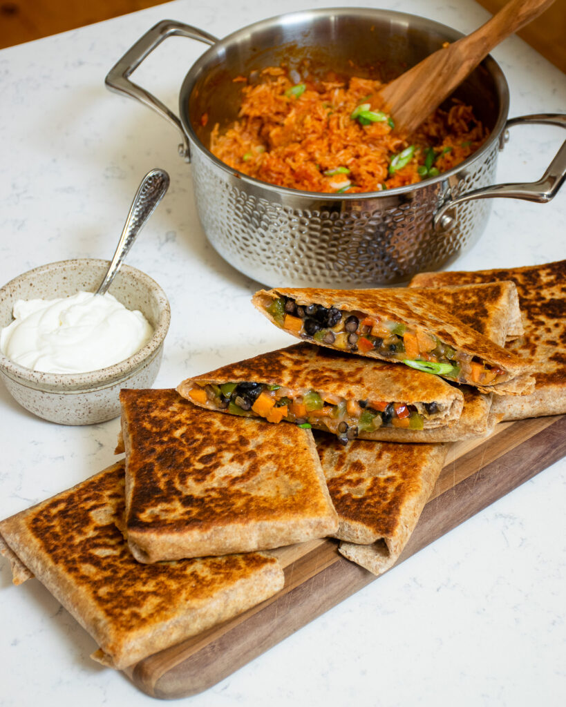 Burrito pockets on a wooden board with a saucepan of Mexican rice in the background.