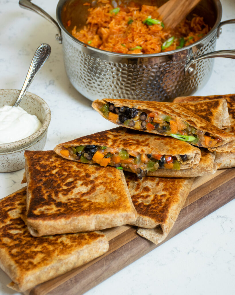 Black bean burrito pockets on a wooden board with a saucepan of Mexican rice in the background.
