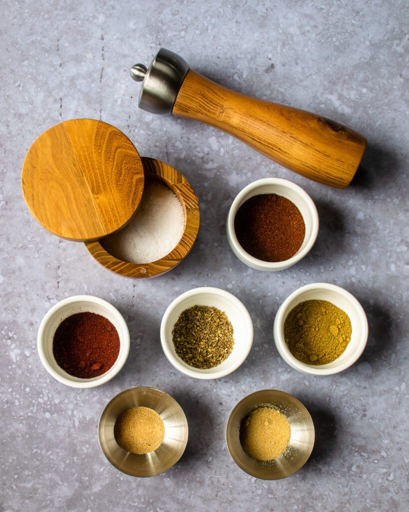 Looking down on small white bowls with spices and a wooden peppermill and salt box.