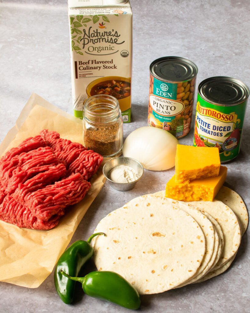 Ingredients for beef tacos: ground beef, tortillas, cheese, spices, stock, canned beans and canned tomatoes.