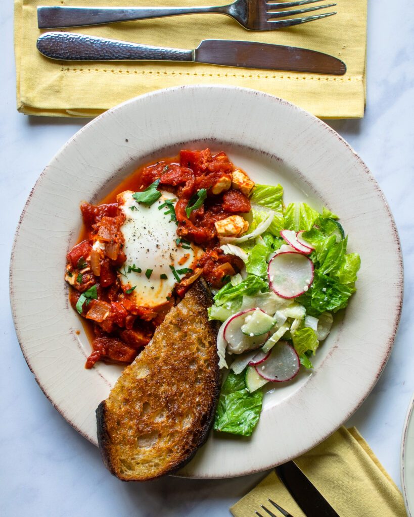 Looking down on one plate of shakshuka with salad and toast.