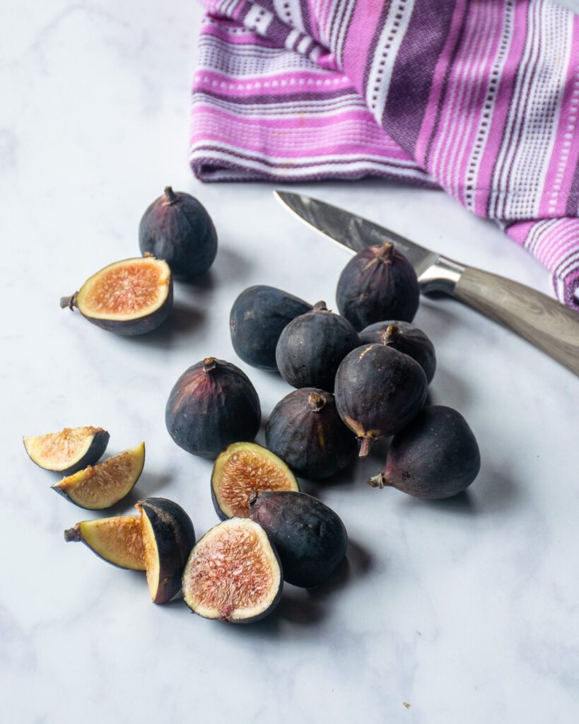 Figs, a paring knife and a purple hand towel on a marble countertop.