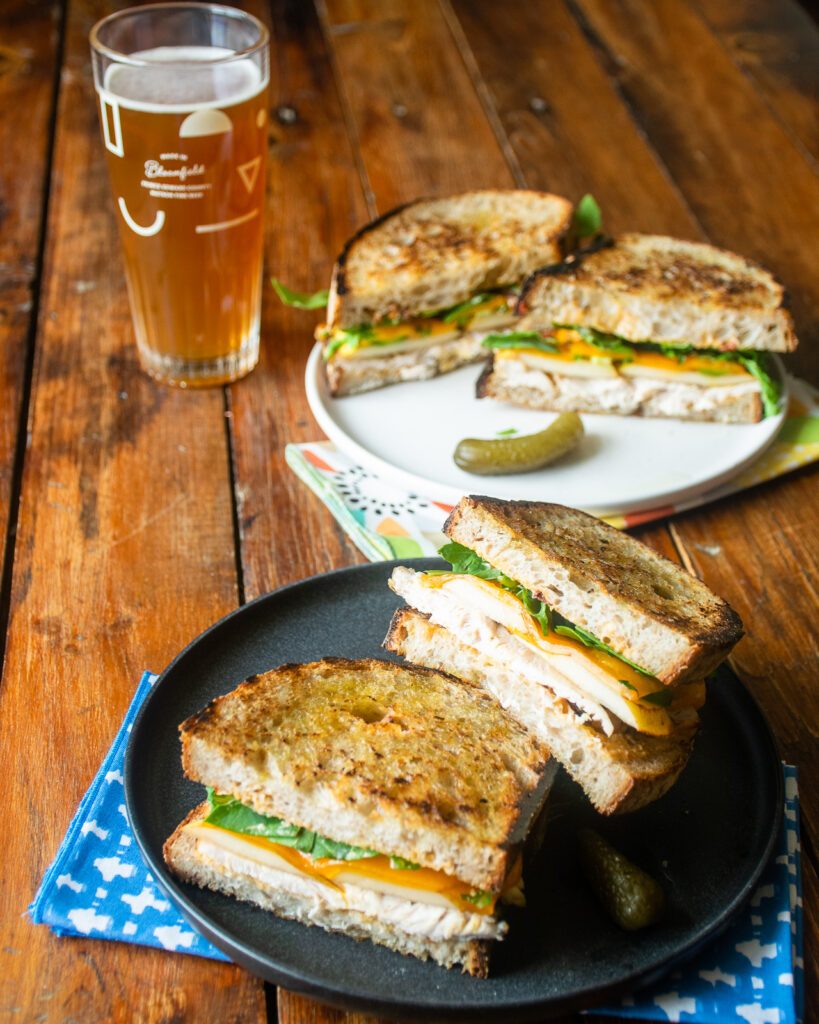 Two spicy turkey paninis on plates with a glass of beer.