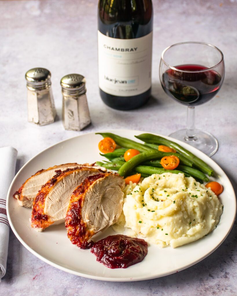 A white plate with a turkey dinner with a glass of wine, bottle of wine, salt and pepper shakers.