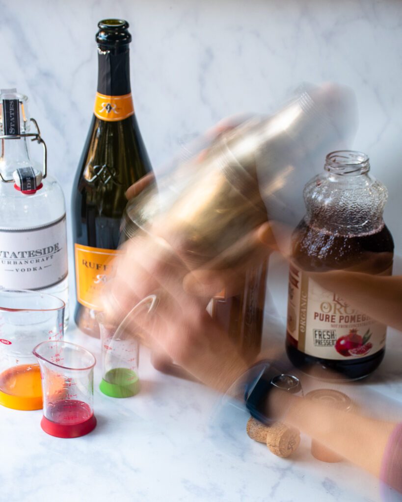 A blur of hands shaking a cocktail shaker with bottles in the background.

