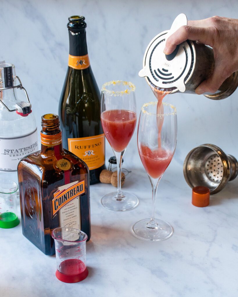 Straining a cocktail from a shaker into two champagne flutes.
