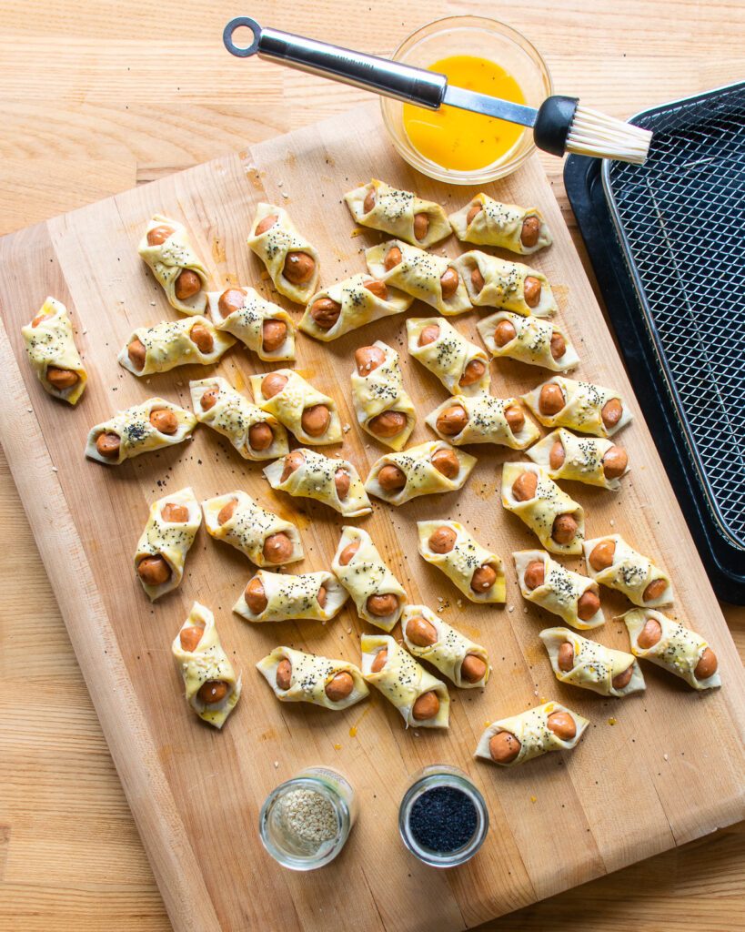 Pigs in a blanket on a cutting board, ready to be baked.