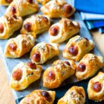 Cheesy Pigs in a Blanket on a serving board with some blue napkins in the background.