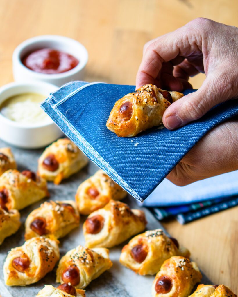 A hand holding a pig in a blanket on a blue napkin.