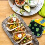 Pork Carnitas tacos on a tray with fixings near by.